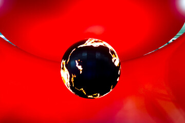 Digital globe. A large, glowing sphere suspended from above against a solid, dark red background. The sphere's surface has a digital or pixelated appearance.