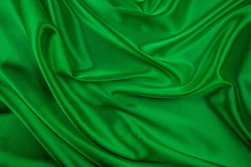 Obraz premium A lush vibrant green satin or silk fabric is draped and folded, creating elegant waves, texture, and highlights perfect for a luxurious abstract background.