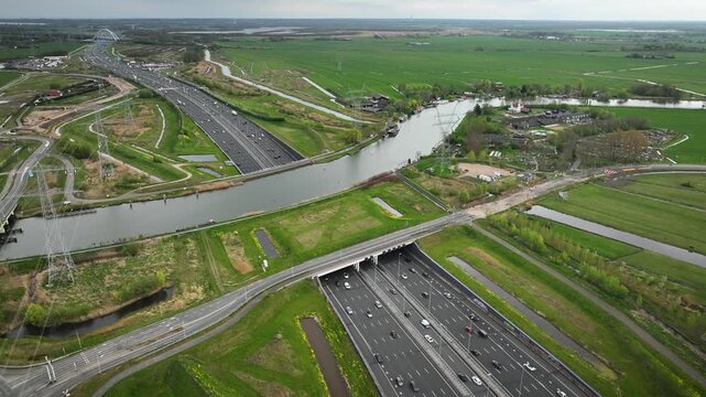 Aerial footage of major multi-lane highway running through underpass beneath Utrechtsche Vecht. Traffic of cars and trucks through sunken roadway while bridges, canals and drainage channels intersect.