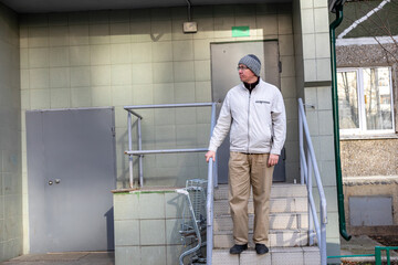 adult man stands on the steps of the entrance to an apartment building, holding onto the metal railing. Concept of everyday life in an urban courtyard. Housing environment.