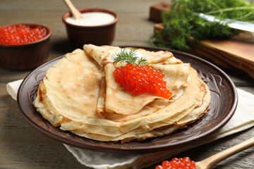 Tasty crepes with red caviar, sour cream and dill on wooden table, closeup