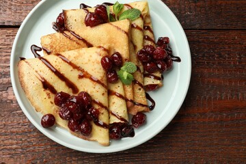 Delicious crepes served with cherry jam and chocolate on wooden table, top view