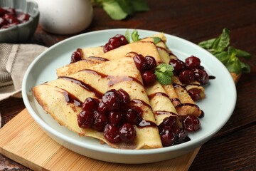 Delicious crepes served with cherry jam and chocolate on wooden table, closeup