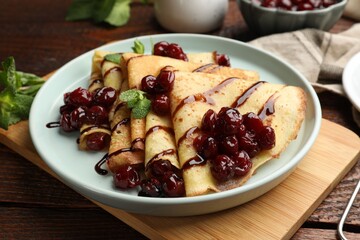 Delicious crepes served with cherry jam and chocolate on wooden table, closeup