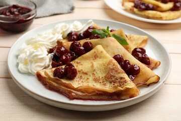 Tasty crepes with cherries, whipped cream and mint served on white wooden table, closeup