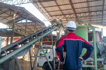 Fototapeta premium Industrial worker observing conveyor system in factory setting with machinery and equipment in background under bright daylight