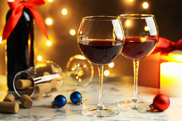 Glasses of red wine, bottle and Christmas decor on light marble table against blurred lights, closeup