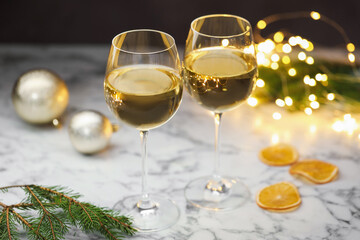 Glasses of white wine and Christmas decor on light marble table, closeup