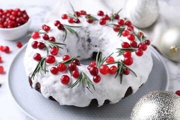 Tasty Christmas cake with cranberries, rosemary and baubles on white table, closeup
