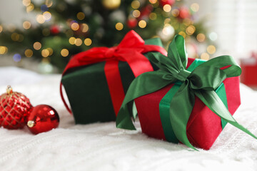Gift boxes and Christmas baubles on bed against blurred lights indoors, closeup