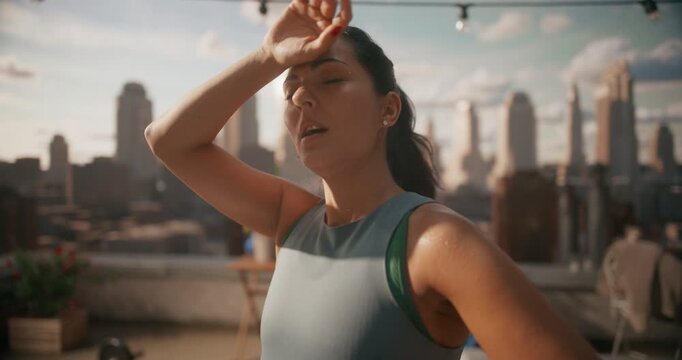 Sweaty Young Woman Stands on a Rooftop Workout Spot, Hands on Hips, Breathing Deeply After Hard Cardio Exercise, Using Outdoor Training to Build Fitness, Heart Health, in the City.