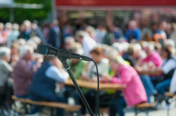 Seitliche Nahaufnahme eines Mikrofons im Halter vor einer Masse an unkenntlichen Menschen im...