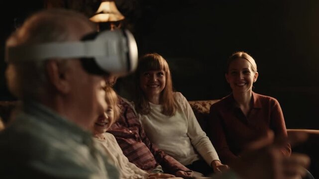 An elderly man wearing a virtual reality headset sits on a couch with family watching and smiling.