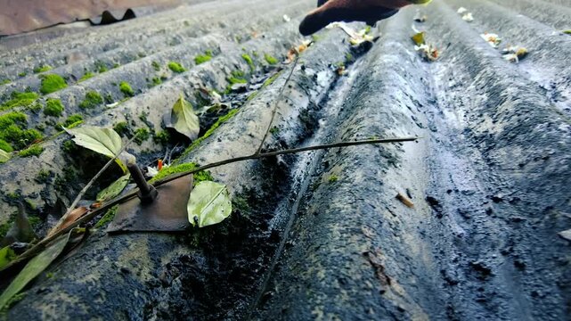 Hand in protective glove cleaning a dirty corrugated roof surface outdoors