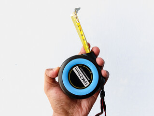 A detailed view of a single hand firmly gripping a retractable metal measuring tape against a smooth white-gray background. Great for tool displays, tutorials, and precision themes.