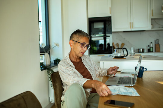 Mature adult man paying bills online at home kitchen, focused