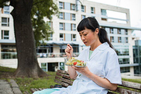 Adult healthcare worker relaxed eating salad on hospital courtyard bench