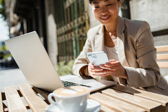 Adult woman smiling while working on smartphone at outdoor cafe - Powered by Adobe