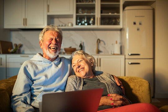 Senior couple laughing while watching laptop on sofa at home