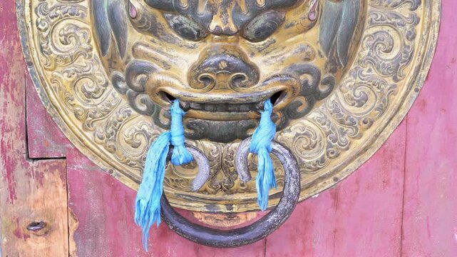 Close-up of a brass door knocker at Erdene Zuu Monastery, Mongolia. The ornate lion head with blue ceremonial scarves highlights the intricate detail of the ancient temple.