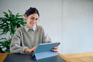 Professional woman wearing glasses smiling while participating in a video call on a tablet, working remotely from home