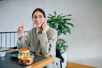 Young woman enjoying her meal while multitasking, engaged in a conversation on her mobile phone at a modern restaurant