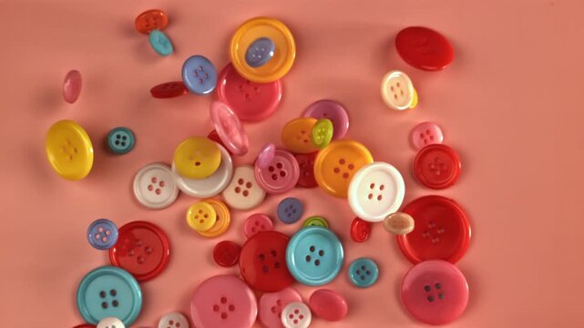 Multi-colored sewing buttons fall on a red table. Filmed on a high-speed camera at 1000 fps. High quality FullHD footage