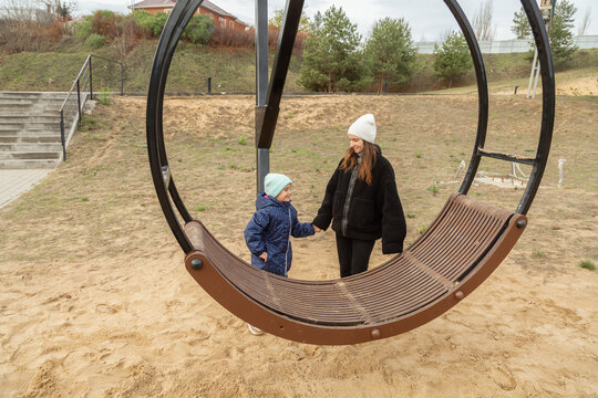 Family day. Happy girl swinging on swings having fun with mother on outdoor playground in park. - Powered by Adobe