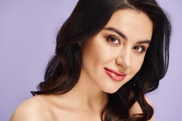 Naklejka premium Young beautiful woman poses gracefully against a soft purple backdrop with a charming smile