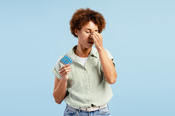 Woman experiencing headache, holding blister pack of pills, feeling pain and stress