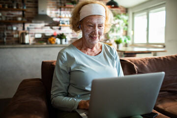 Senior woman smiling with face mask using laptop at home