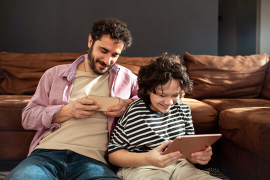 Adult father and child son smiling with smartphone and tablet at home