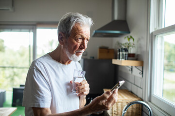 Senior man checking smartphone with concerned expression in home kitchen