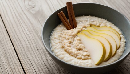 Warm porridge with pear and cinnamon sticks in a bowl. Healthy and wholesome oatmeal breakfast on a rustic wooden table