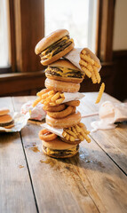 Tower of fast‑food items including burgers, fries and onion rings arranged in a playful vertical stack on a rustic wooden table, highlighting indulgent comfort food concept with humor