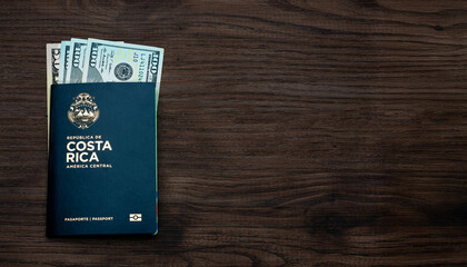 Costa Rica passport partially filled with US dollar banknotes on dark wooden surface, symbolizing travel and finance.