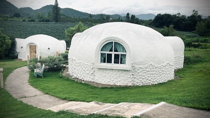 Ratchaburi, Thailand :Beautiful architecture of white dome bungalow with arch window and door linked by a walkway on lush green lawn at IGLOO Suanphueng resort.