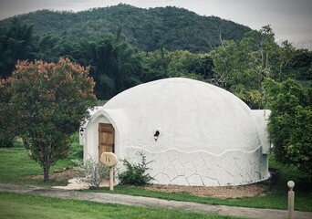 Ratchaburi, Thailand :Beautiful architecture of white dome bungalow with arch window and door linked by a walkway on lush green lawn with mountain view at IGLOO Suanphueng resort.