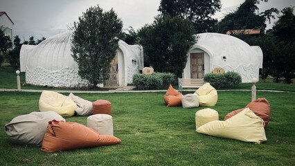 Ratchaburi, Thailand : Unique dome shaped resort among green tree, featuring a grassy lawn with colorful bean bags for relaxation at IGLOO Suanphueng resort.