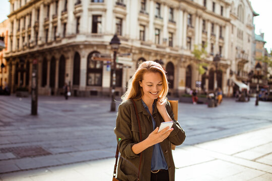 Young adult woman smiling at smartphone on historic city street