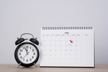 Alarm clock beside a desk calendar with a marked date in April, symbolizing scheduling, time management, reminders, deadlines, planning, and organizing important events in daily work or personal life.