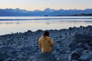 Lake Pukaki, NZ - May 24, 2025 (Twilight): A figure in a yellow hoodie sits on a rocky shoreline,...