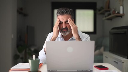 Stressed businessman experiencing headache while working on laptop - Powered by Adobe