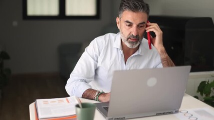 Mature businessman talking on phone while working from home office - Powered by Adobe