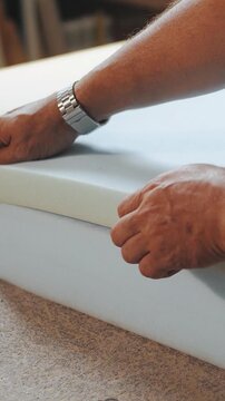 Vertical video. Worker glues foam for the production of upholstered furniture. Factory for the production of sofas and armchairs. Close-up of hands.