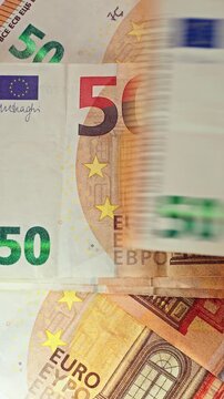 Vertical close-up: Euro banknotes falling onto a table in a scattered arrangement, representing cash flow, wealth, abundance, financial prosperity, and money movement concepts.
