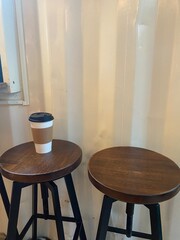 Paper coffee cup on wooden stool in minimalist cafe interior