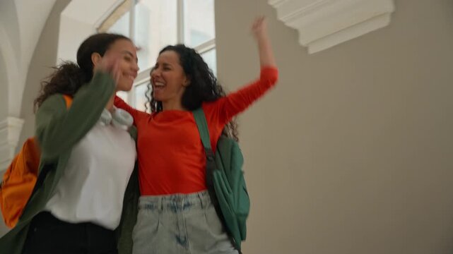 Two multiracial happy girls students dancing walking university corridor women friends multiethnic females diversity Hispanic Latina going in college academy hall good carefree mood pass exam study