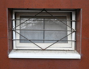 Window with security bars on a brick wall showing signs of wear and dust near a residential area