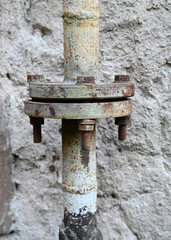 Close-up of rusty metal pipe connection with worn bolts against a textured wall